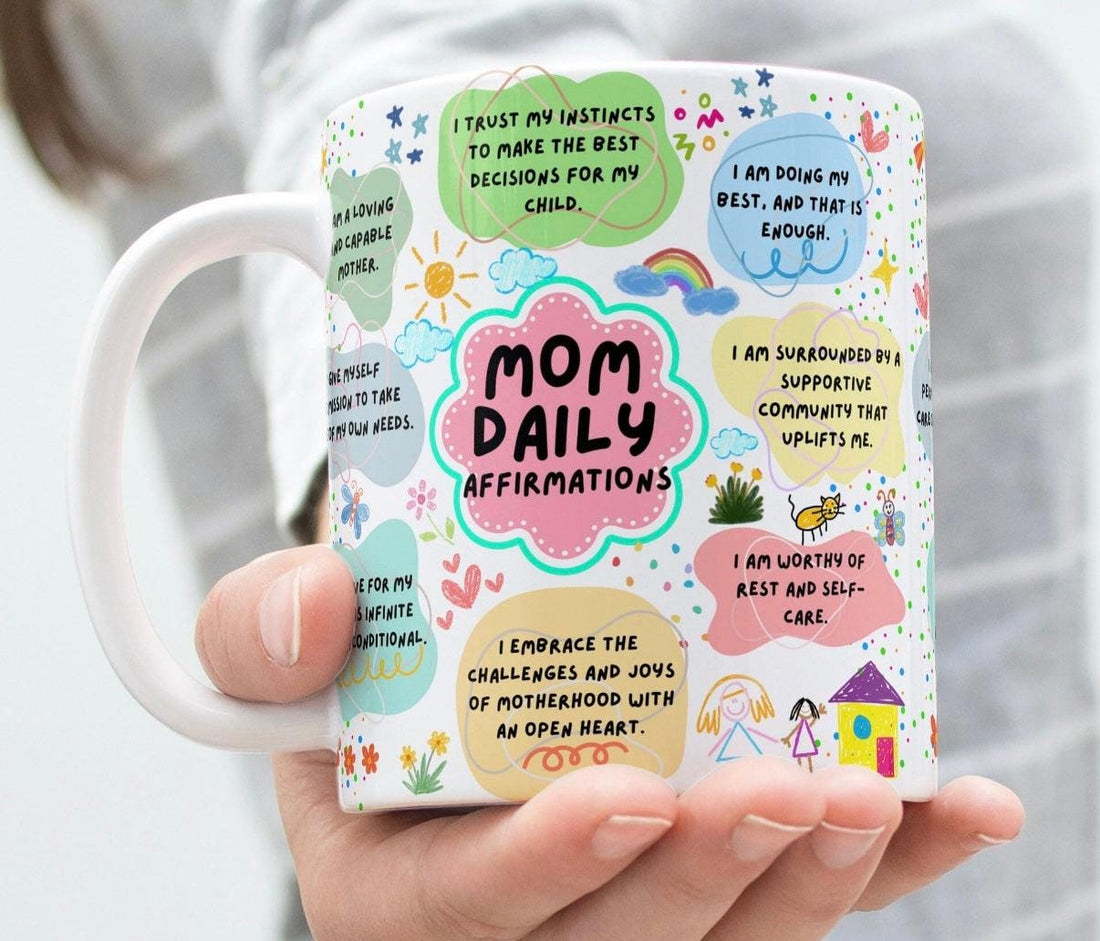 White ceramic mug with colorful Mom Daily Affirmations print next to tea