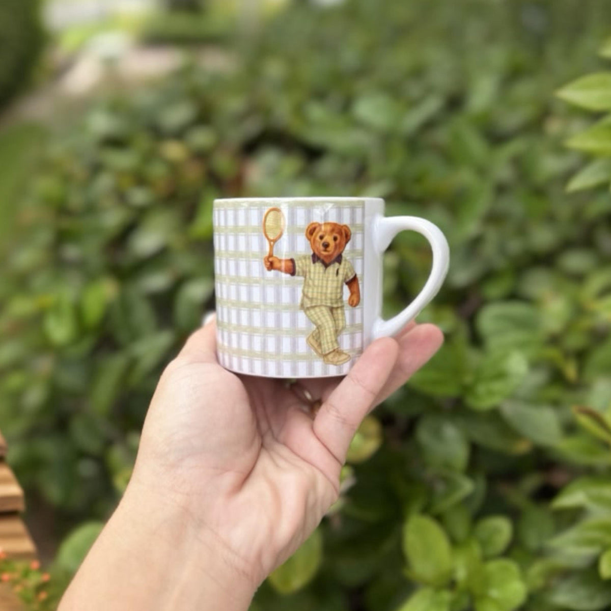 Tennis bear espresso mug with gingham pattern, held outdoors