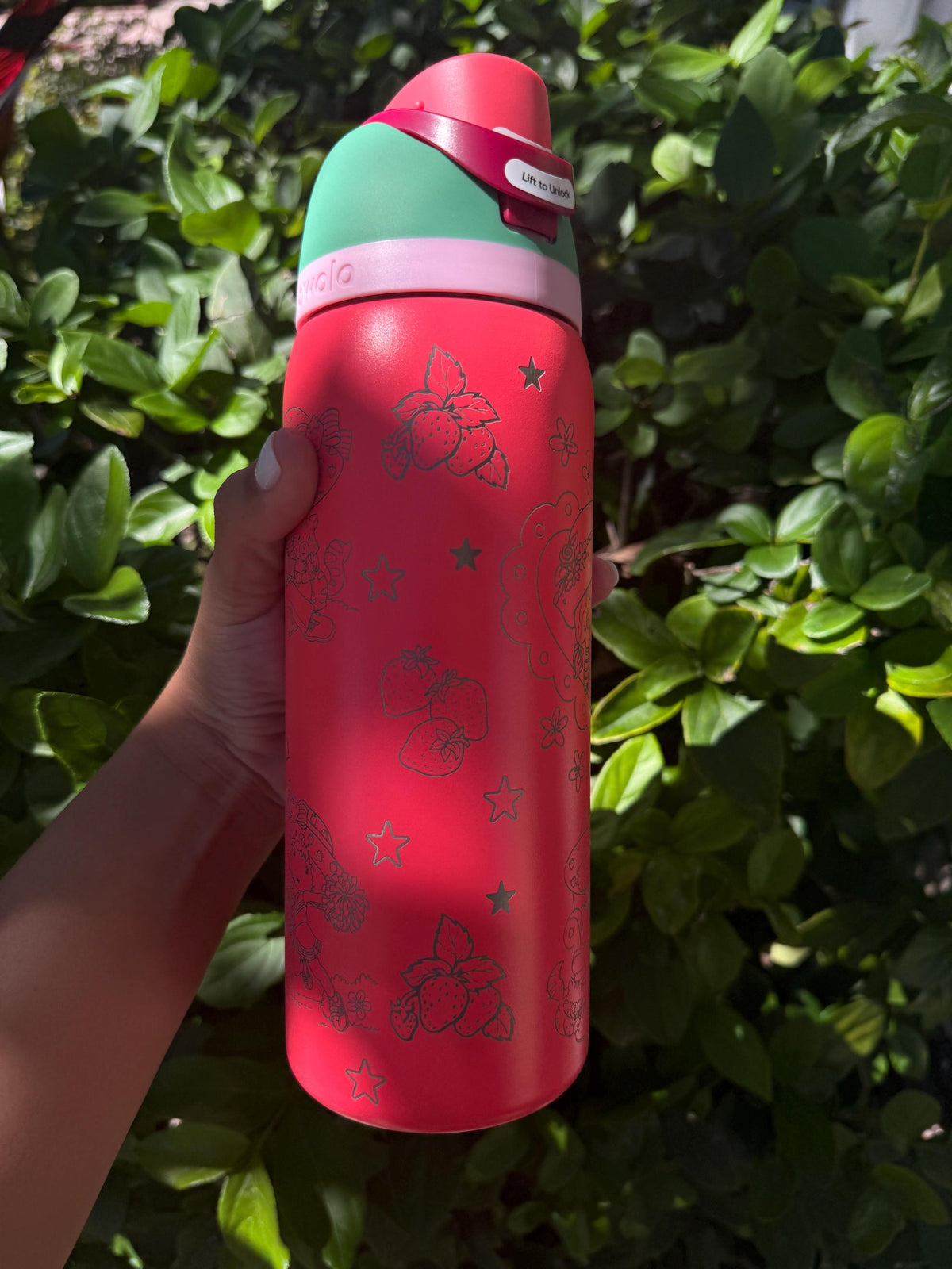 Pink engraved Owala held outdoors in front of greenery