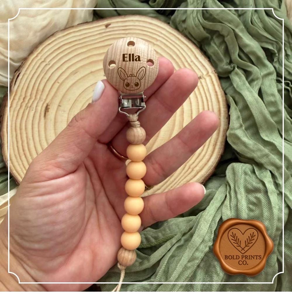 Peach silicone pacifier clip with an engraved beechwood name