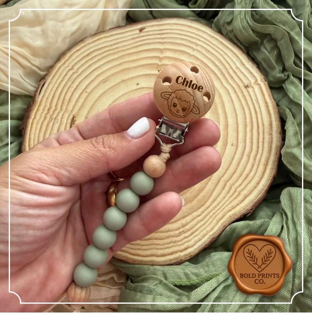 Sage and cream beaded pacifier clip held in hand