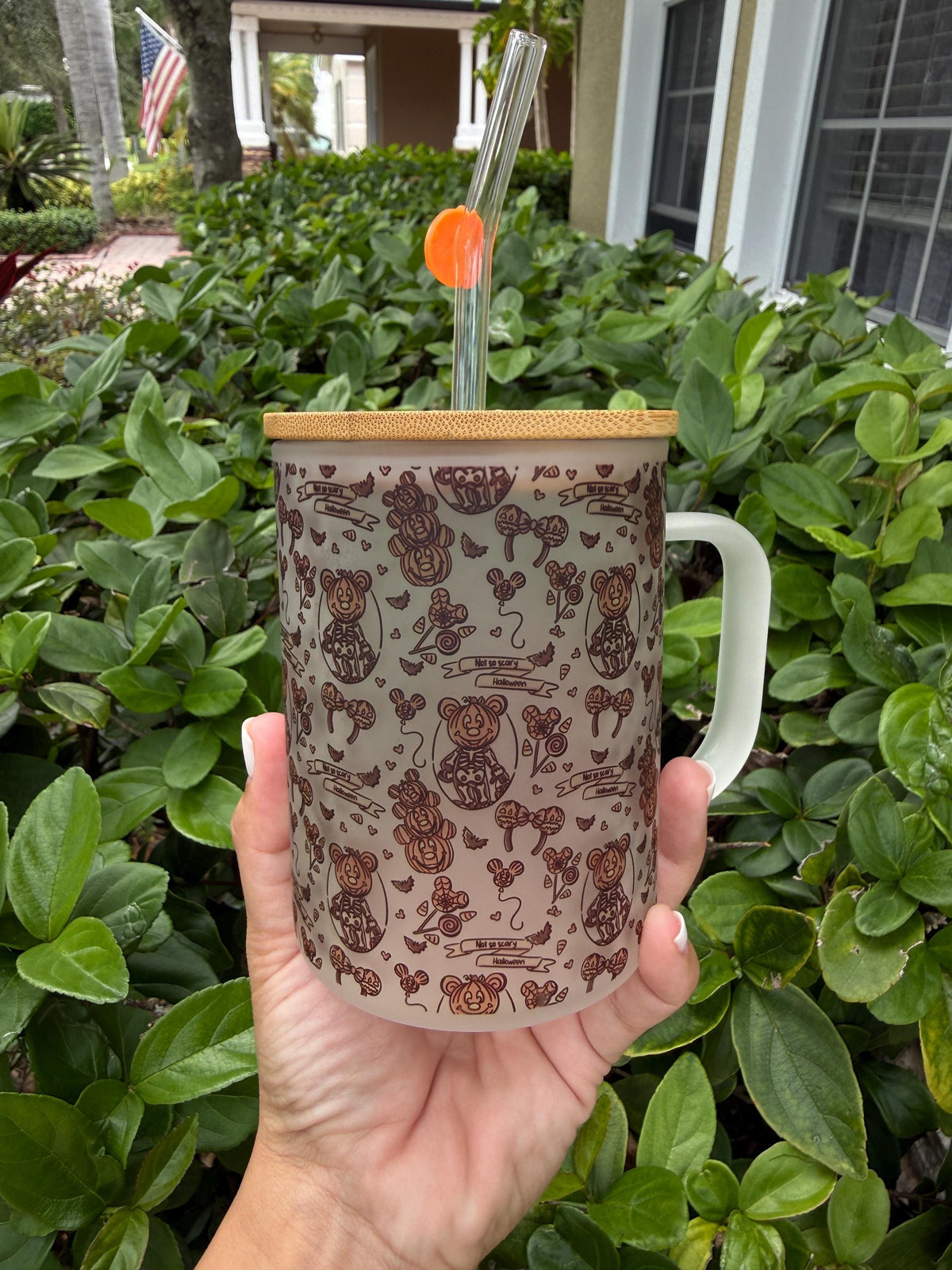 Halloween glass cup with handle and pumpkin straw, held outdoors