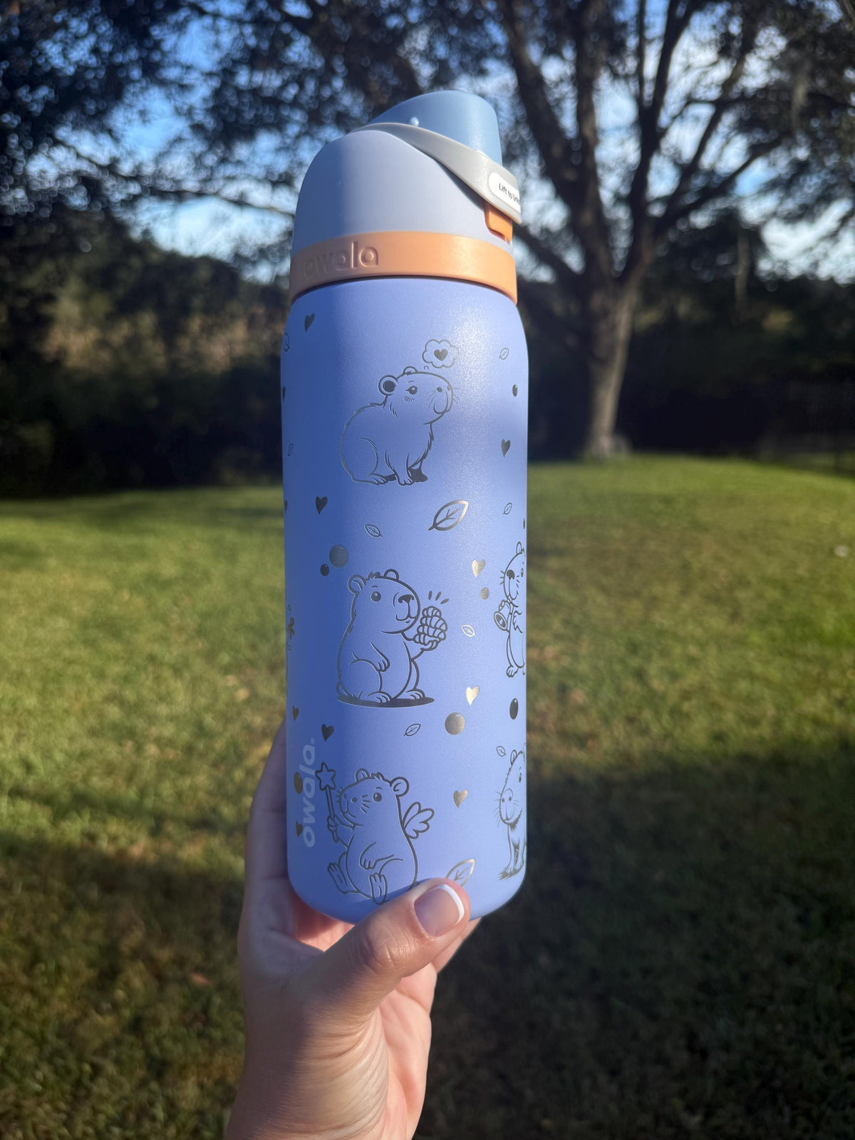 Capybara engraved Owala FreeSip with orange lid, held outdoors