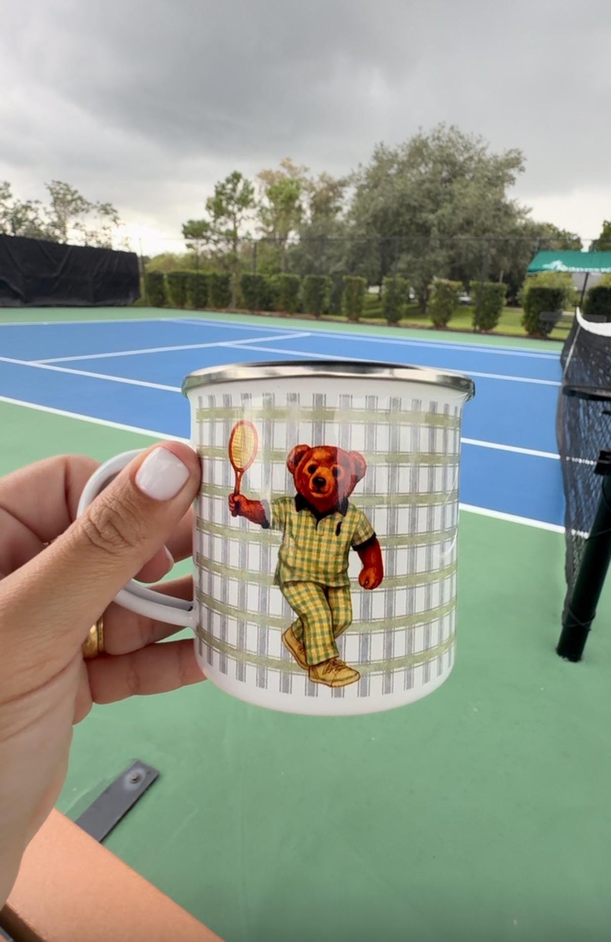 Tennis bear mug held in front of a tennis court