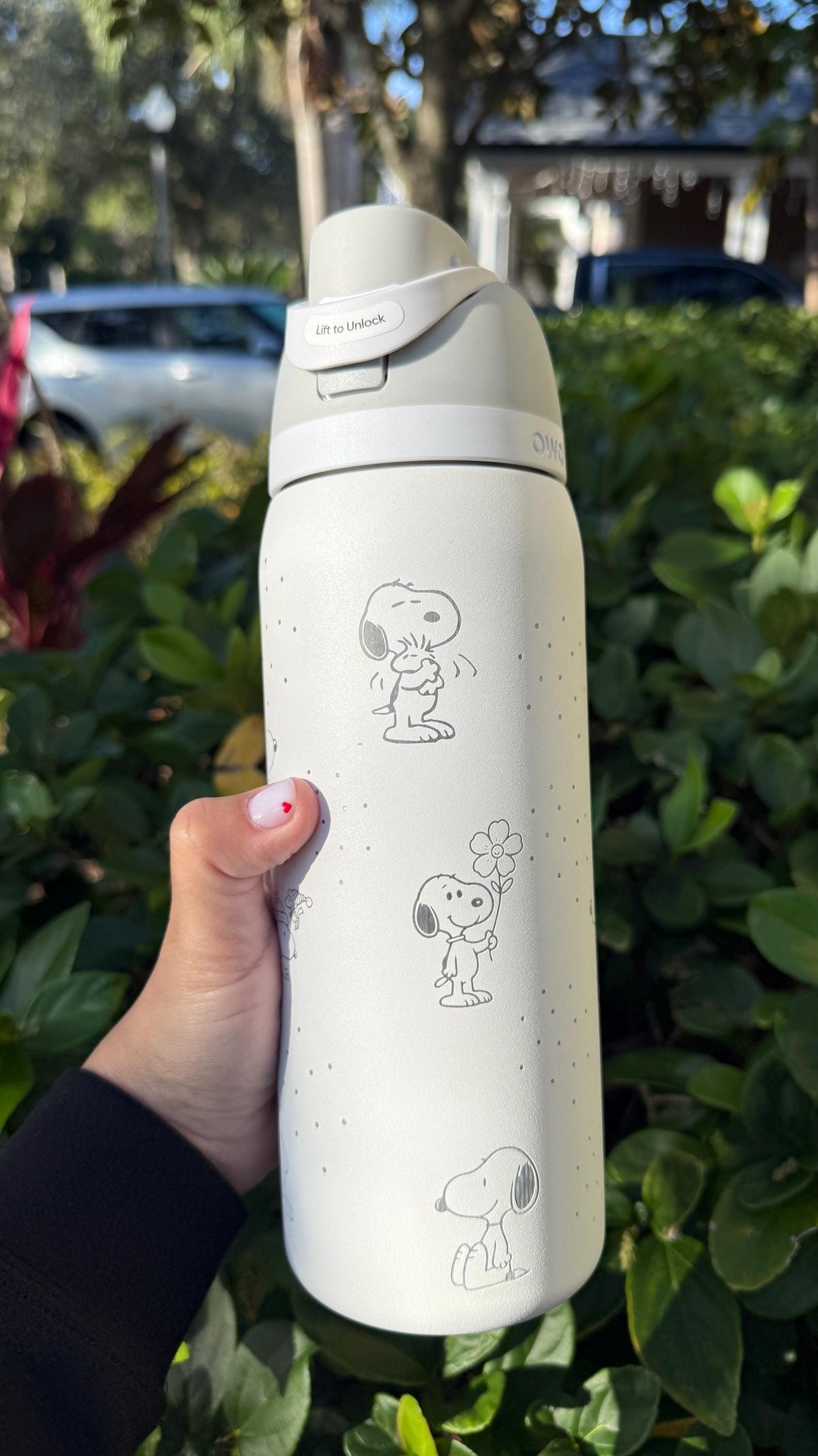 Cream engraved Owala FreeSip with Snoopy artwork, held outdoors