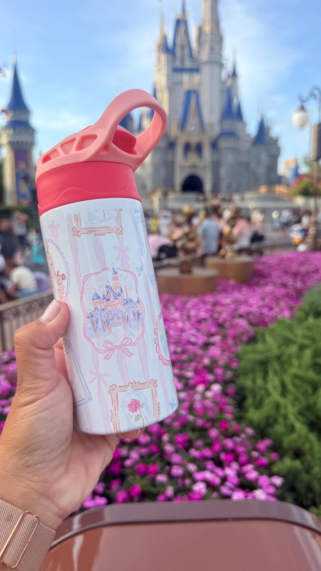 White 12 oz kids water bottle with pink lid and castle design, in front of a castle