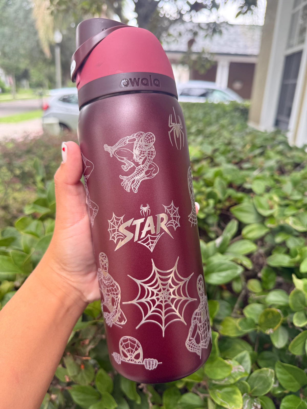 Close-up of spider web and name engraving on a burgundy Owala FreeSip
