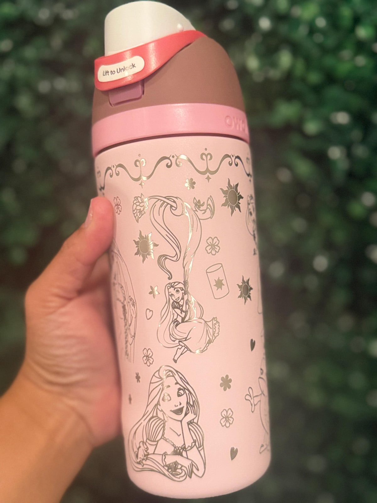 Pink Owala FreeSip with a Rapunzel-inspired laser engraving, held outdoors